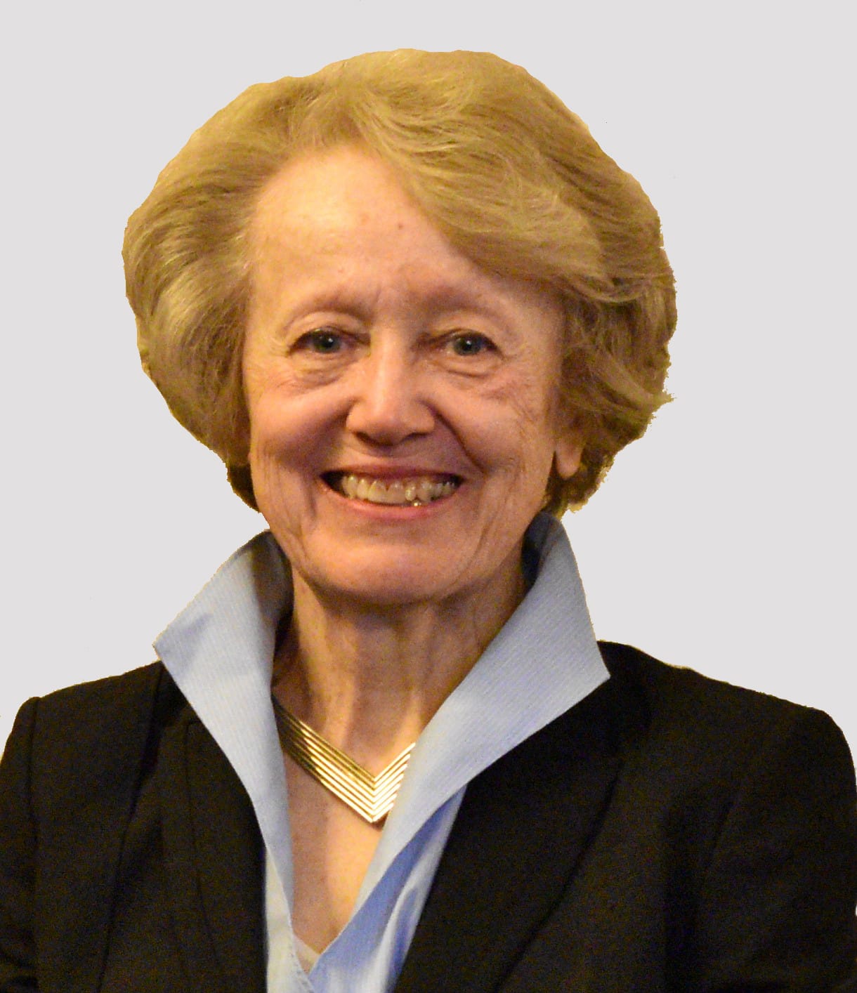 Portrait of an older woman with blonde hair wearing a black blazer and gold necklace, smiling.